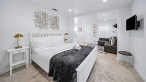 A modern bedroom with a white bed, a black throw blanket, a bedside lamp, and a wall-mounted TV. - Tropical Grove Bay 1/1 | Newly Renovated Escape (Miami)