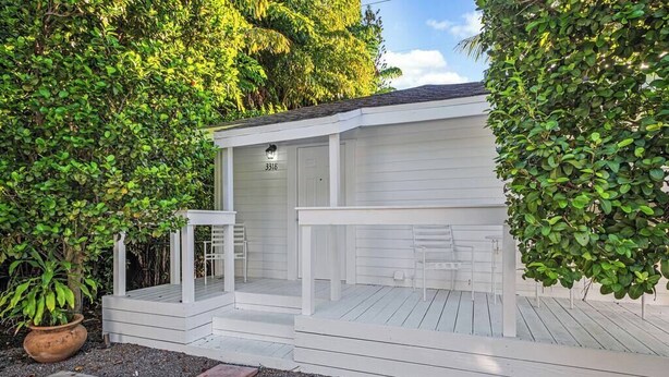 A white wooden structure with a porch, a door labeled "3318", and a small table and chair on the porch. - Tropical Grove Bay 1/1 | Newly Renovated Escape (Miami)