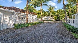 A gravel driveway leading to a row of white buildings with a tropical backdrop. - Tropical Grove Bay 1/1 | Newly Renovated Escape (Miami)