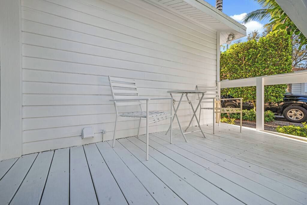 Un terrazzo in legno bianco con tavolo e sedie, una zona coperta e un veicolo sullo sfondo.