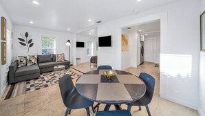 A modern living room with a sofa, a dining table with chairs, a flat-screen TV mounted on the wall, and a patterned rug. - Tropical Grove Bay 1/1 | Newly Renovated Escape (Miami)