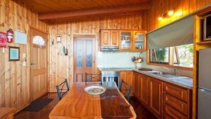 Een houten cabin met daarin een eettafel, stoelen, een keuken voorzien van houten kastjes, een koelkast en een raam met uitzicht.