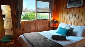 Een slaapkamer met houten lambrisering, een bed, kussens, een nachtkastje en een raam met gordijnen.