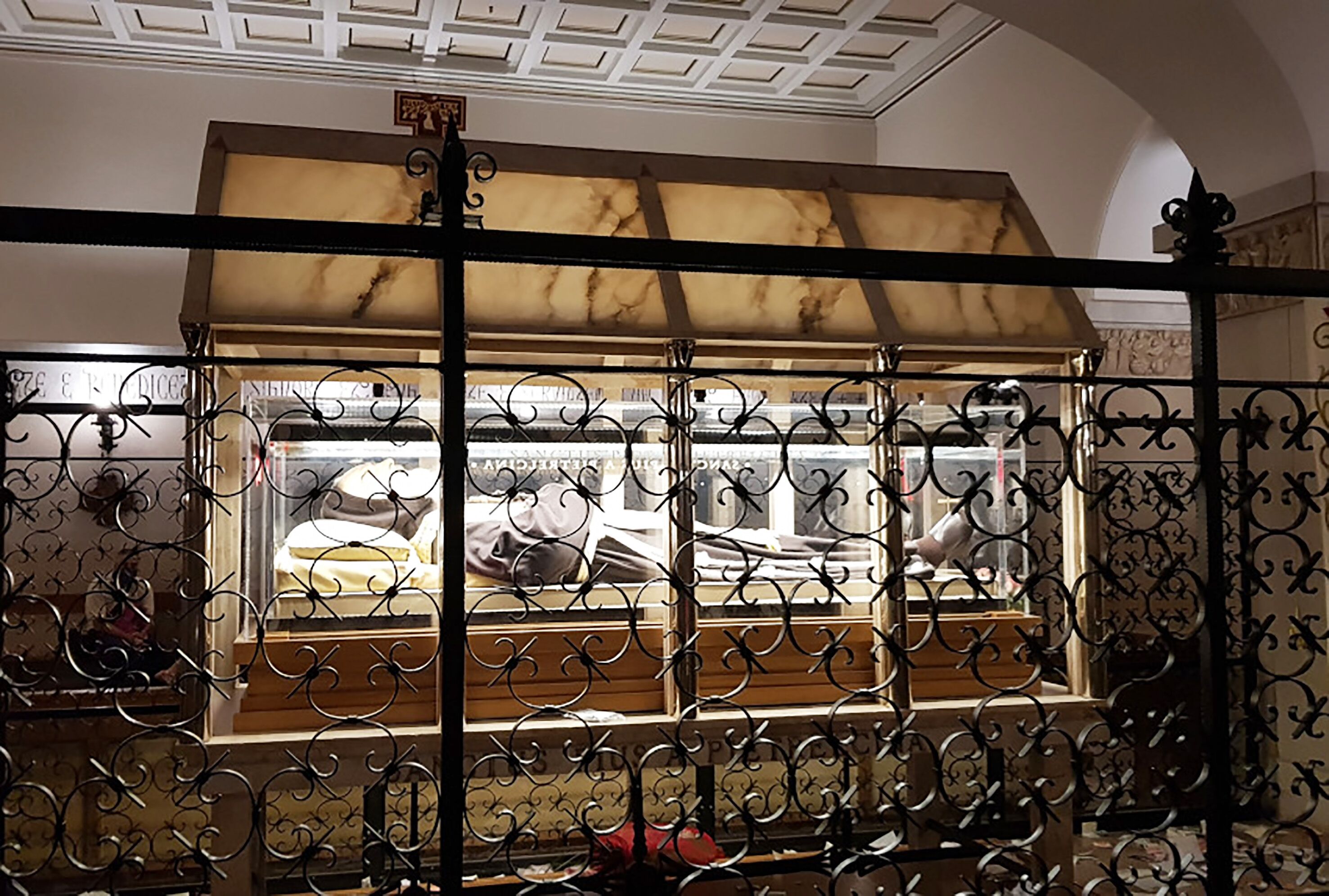 Una stanza con una testiera a motivo marmorizzato, una finestra con ringhiere in ferro decorativo e un soffitto con un disegno geometrico.