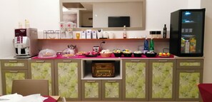 Habitación de hotel con kitchenette, que incluye cafetera, refrigerador y diversos alimentos sobre la encimera.