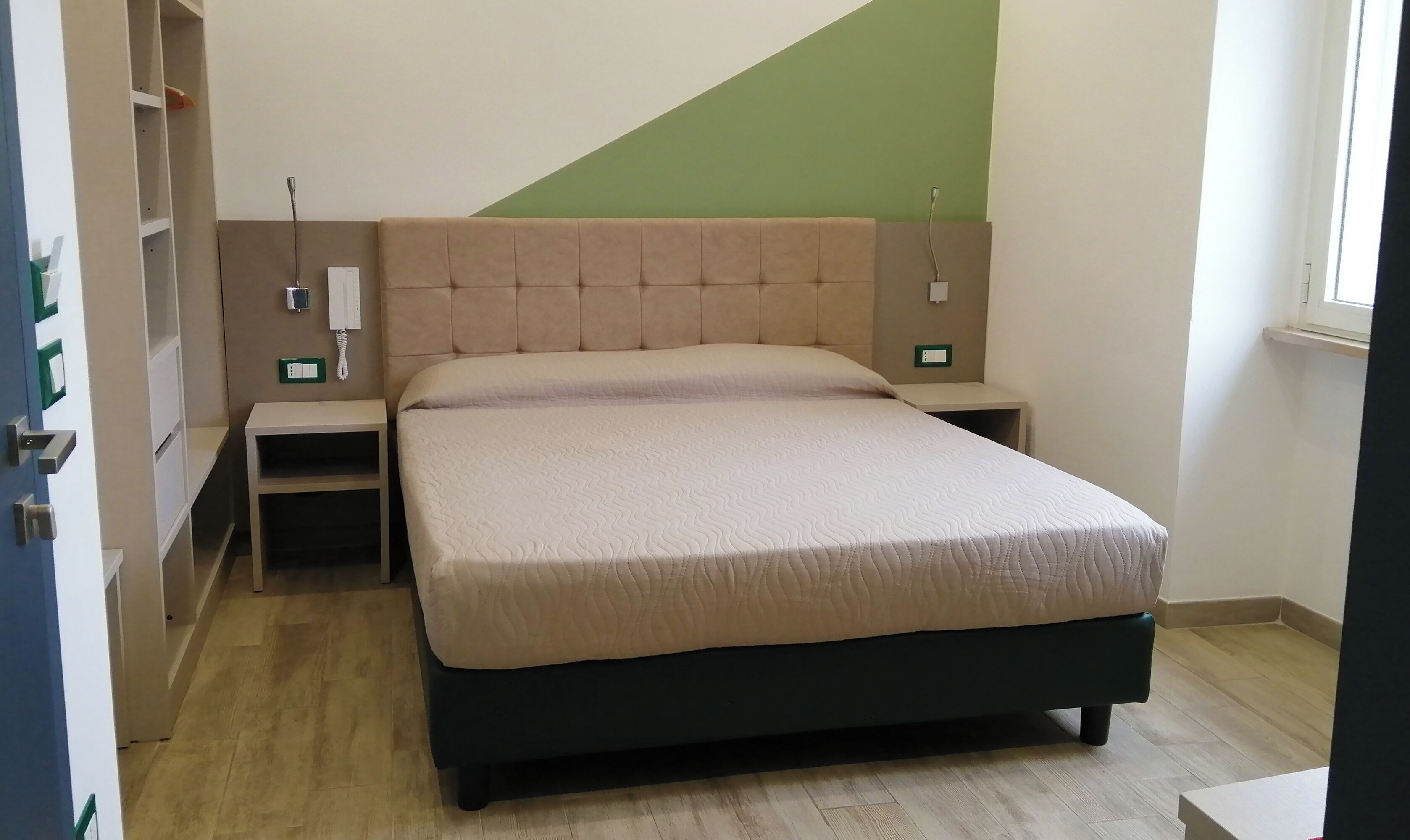 Une chambre à coucher bien aménagée, avec un lit, des tables de chevet et un mur d’accent de couleur verte.