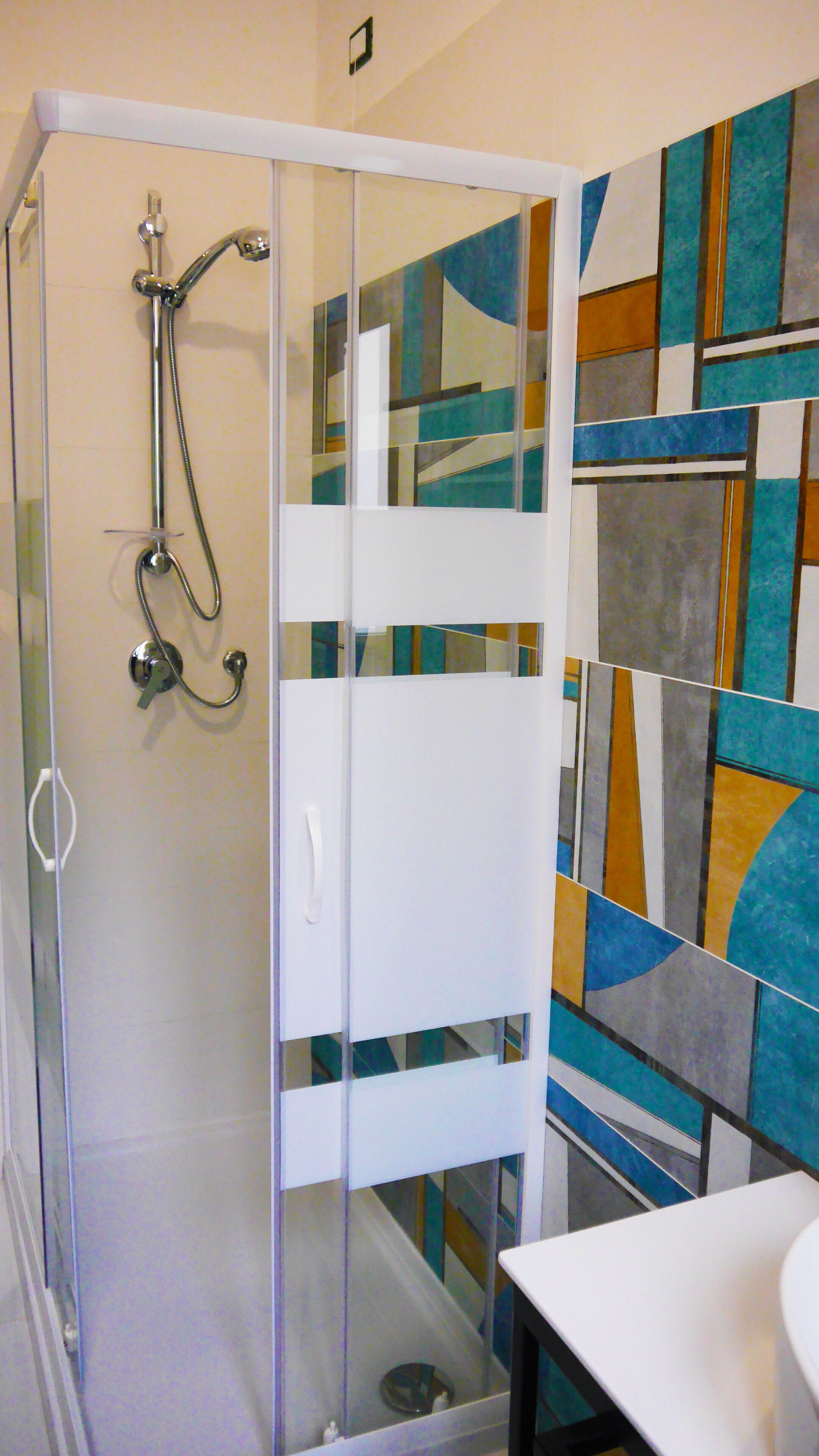 A shower enclosure with a glass door, a white sink, and a tiled wall with abstract patterns.