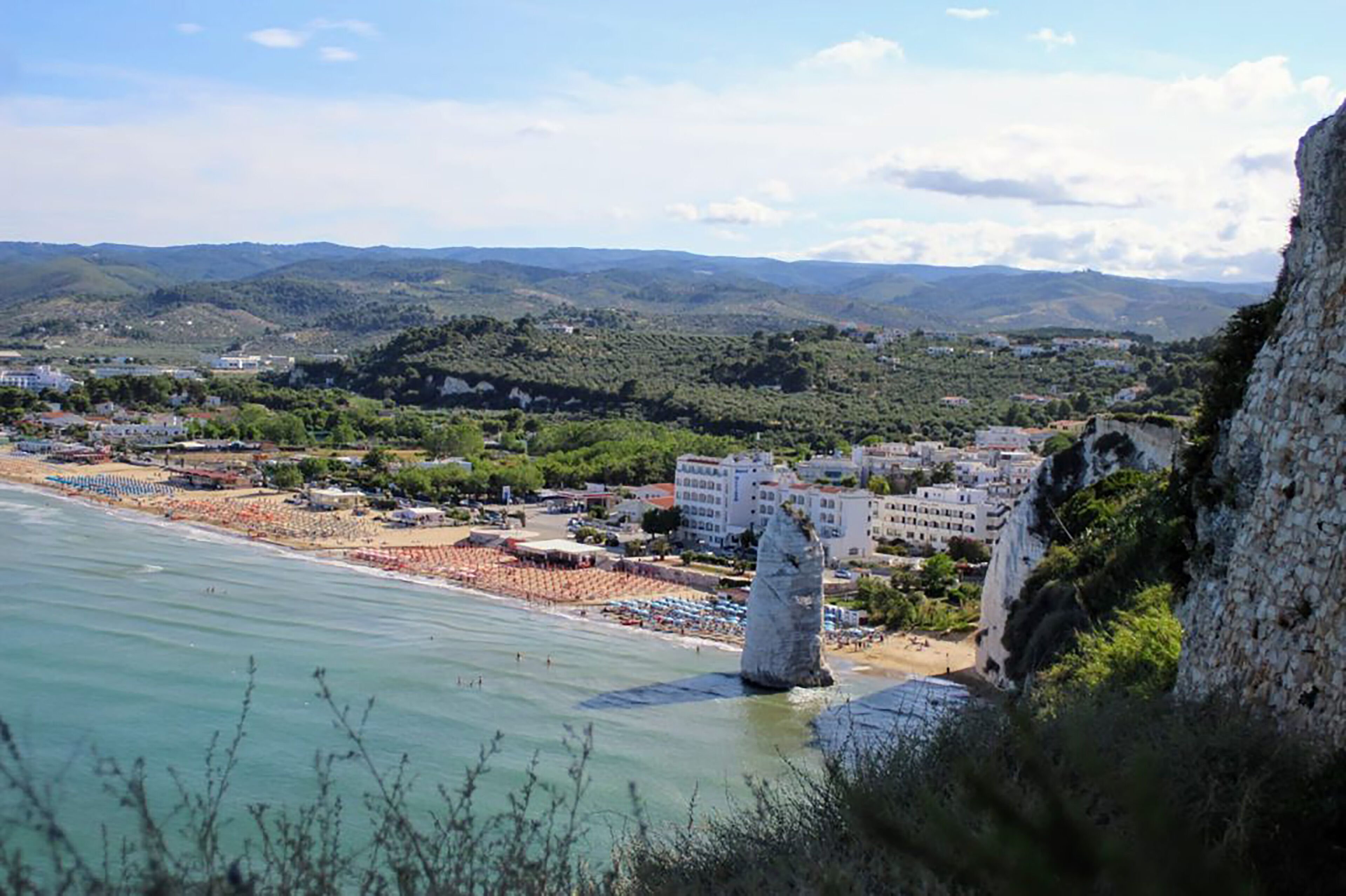 Un pueblo costero con una playa, edificios y una destacada formación rocosa.