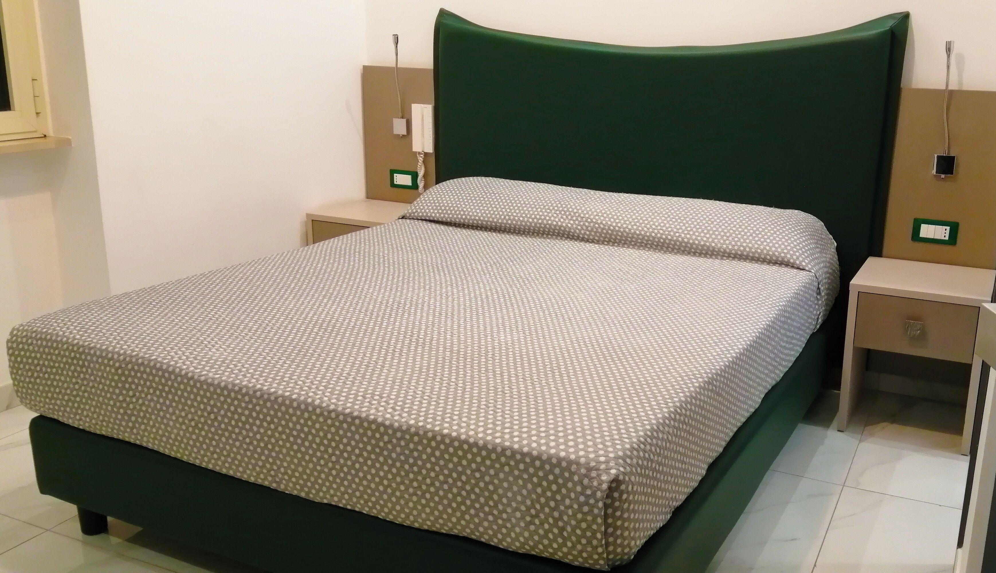 A neatly made bed with a polka dot bedspread, a green upholstered headboard, and two bedside tables with lamps.