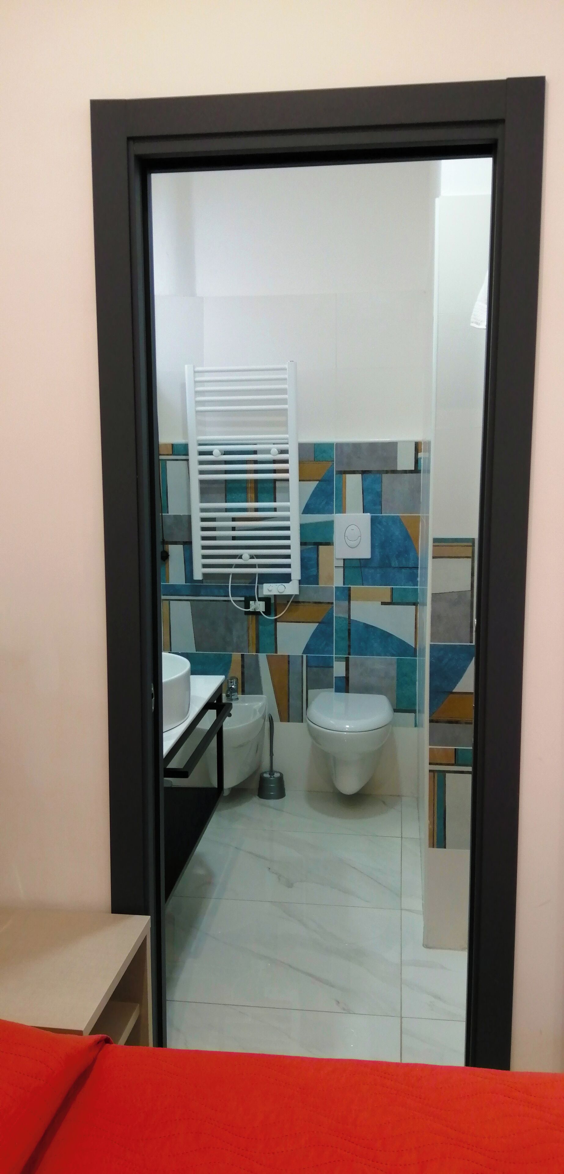 Um banheiro com vaso sanitário branco, pia e porta-toalhas. As paredes são revestidas com um padrão geométrico.