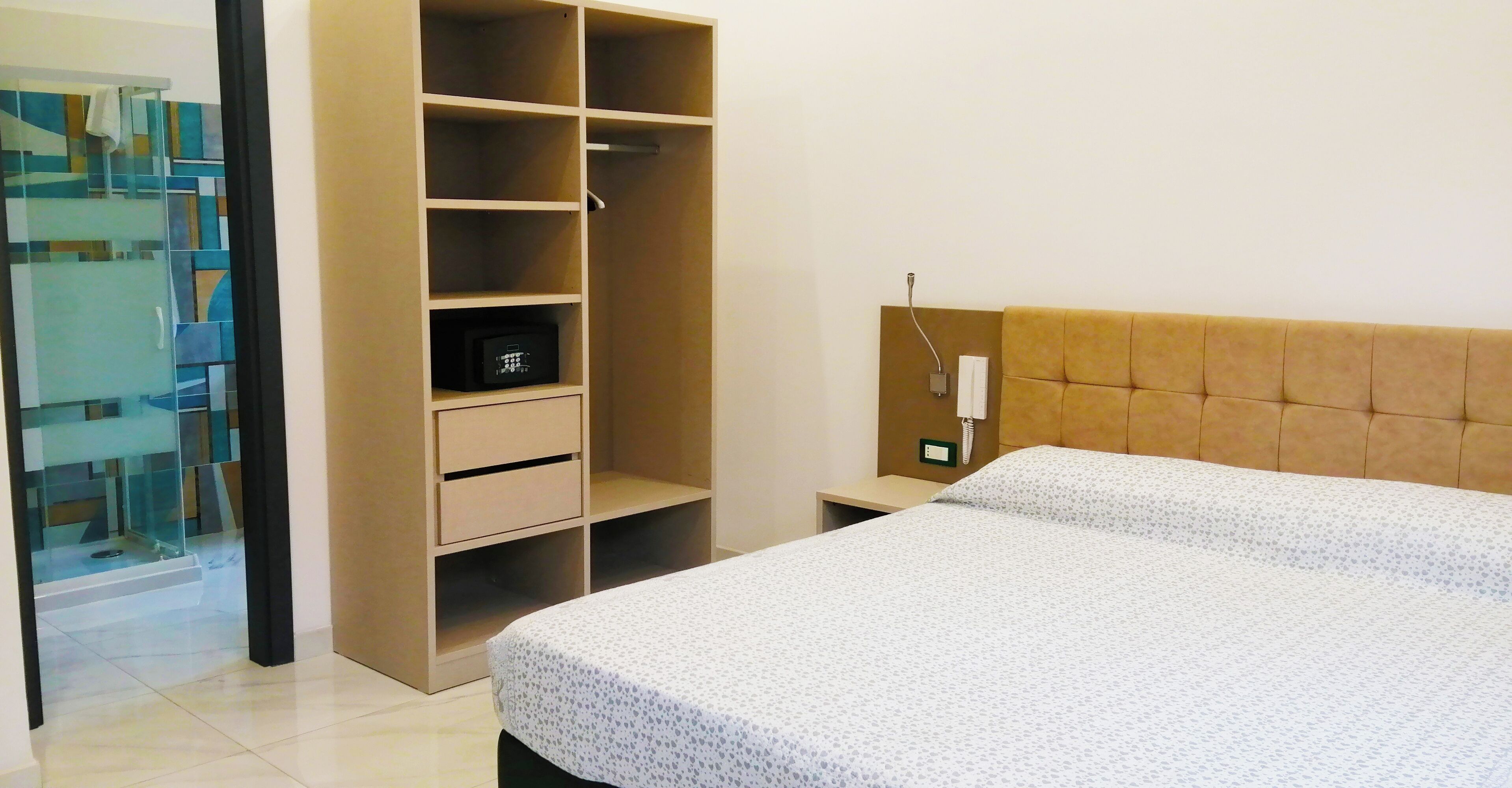 A bedroom with a bed, a wardrobe, and a bedside table with a phone.