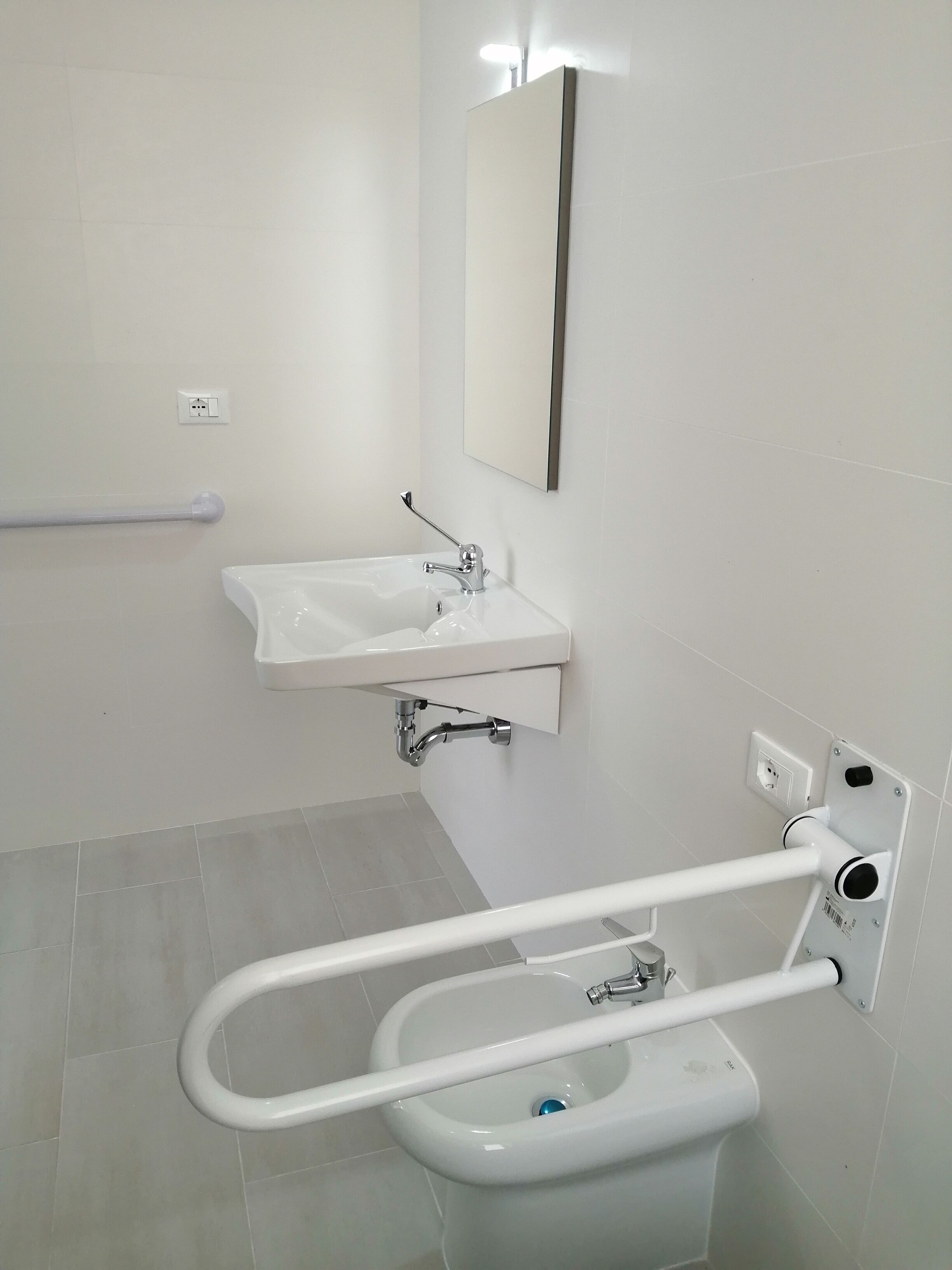 A bathroom with a white sink, a mirror, and a white toilet with a grab bar.