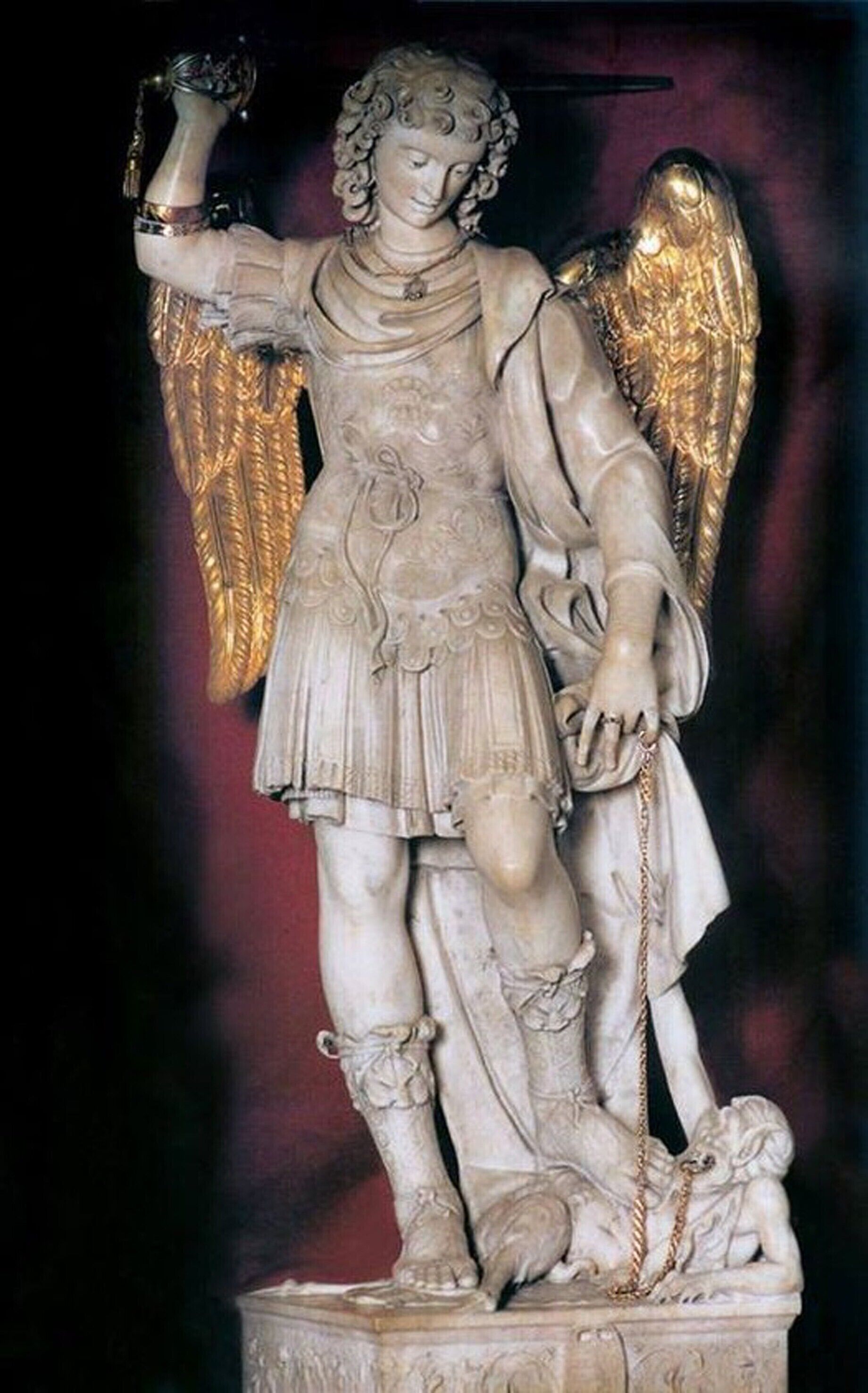 Eine Statue einer geflügelten Figur mit Speer, auf einem Sockel stehend.