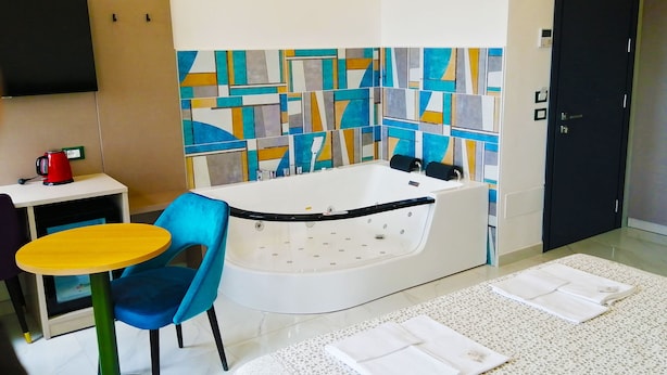 A modern bathroom with a bathtub, a small table with a kettle, and a blue chair. - HOTEL HOUSE GARGANO (San Giovanni Rotondo)