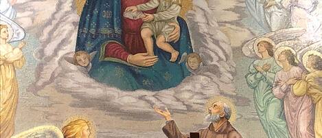 Un mural religioso con una figura central de una mujer sosteniendo un niño, rodeado de ángeles y una cruz.