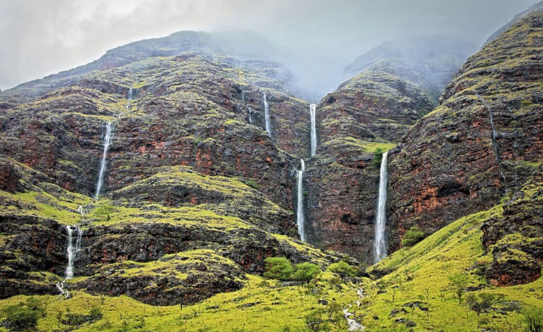 A mountainous landscape with multiple waterfalls cascading down rocky slopes.