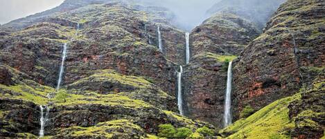 A mountainous landscape with multiple waterfalls cascading down rocky slopes.