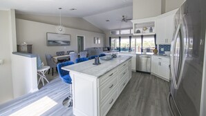 A spacious kitchen with a large island, white cabinetry, and a stainless steel refrigerator. - Capri Charm Remodeled Oasis w/ Heated Pool-Kayaks (Naples)