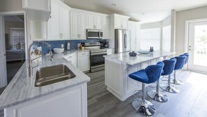 A modern kitchen with white cabinets, a stainless steel refrigerator, a microwave, and a large island with bar stools. - Capri Charm Remodeled Oasis w/ Heated Pool-Kayaks (Naples)