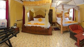 Une chambre avec deux lits, chacun doté d’un baldaquin, une chaise en bois, une petite table et une valise.