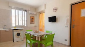 Een kleine keuken met een wasmachine, een eettafel met stoelen, een aan de muur bevestigde televisie en een deur met een bericht.