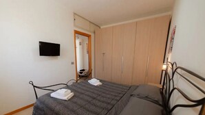 Een slaapkamer met een bed, een aan de muur bevestigde televisie, een kledingkast en een spiegel.