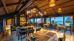 A restaurant with multiple tables and chairs, a ceiling with hanging lights, and a view of the sea. - The Linh Seaside Villa Hoi An (Da Nang)