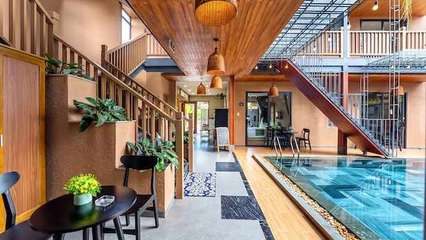 A modern indoor swimming pool area with a wooden ceiling, black and white tiled flooring, and a glass-enclosed upper level. - The Linh Seaside Villa Hoi An (Da Nang)