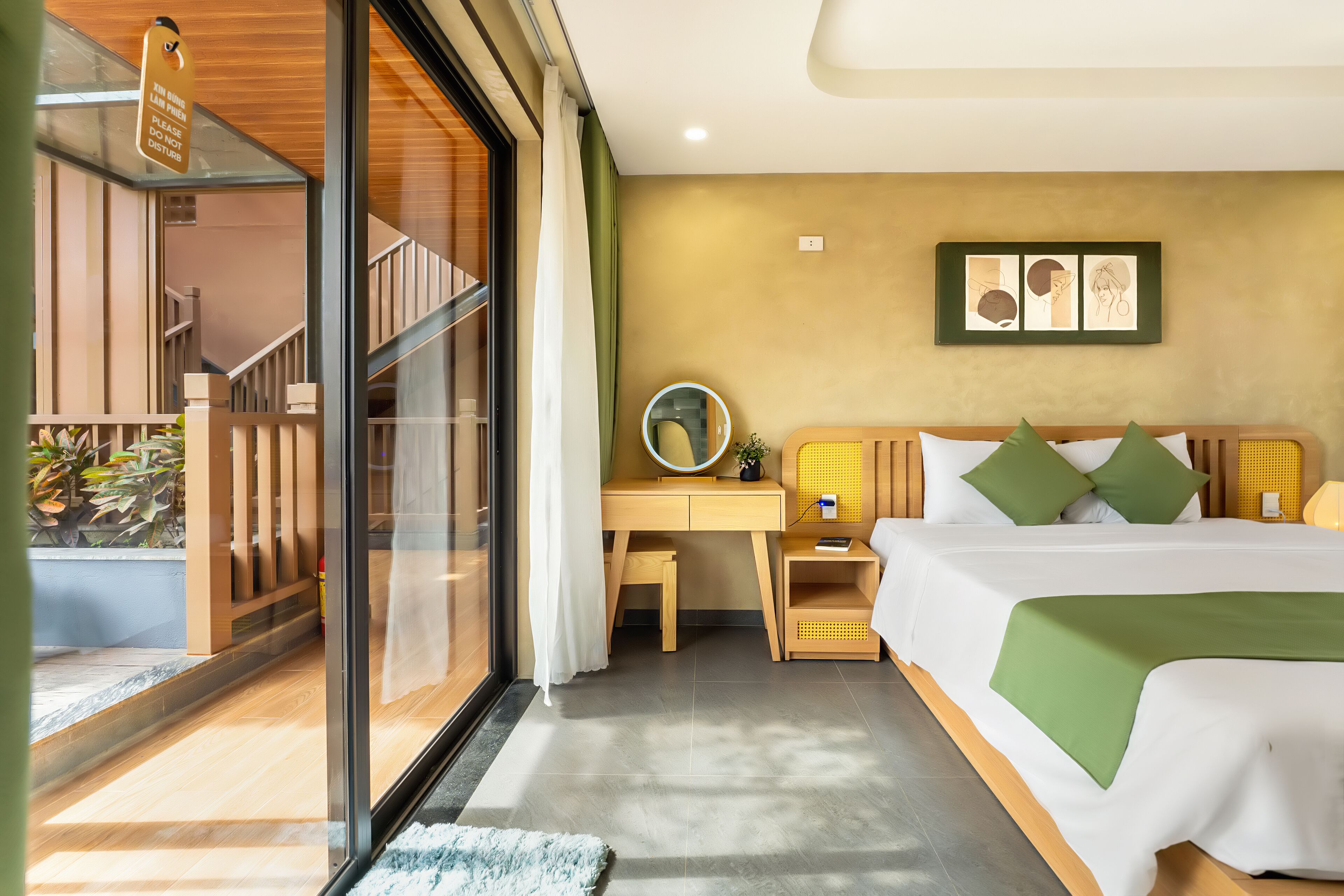 Una camera d'albergo con un letto, un comodino, una scrivania e vista su un balcone con piante.