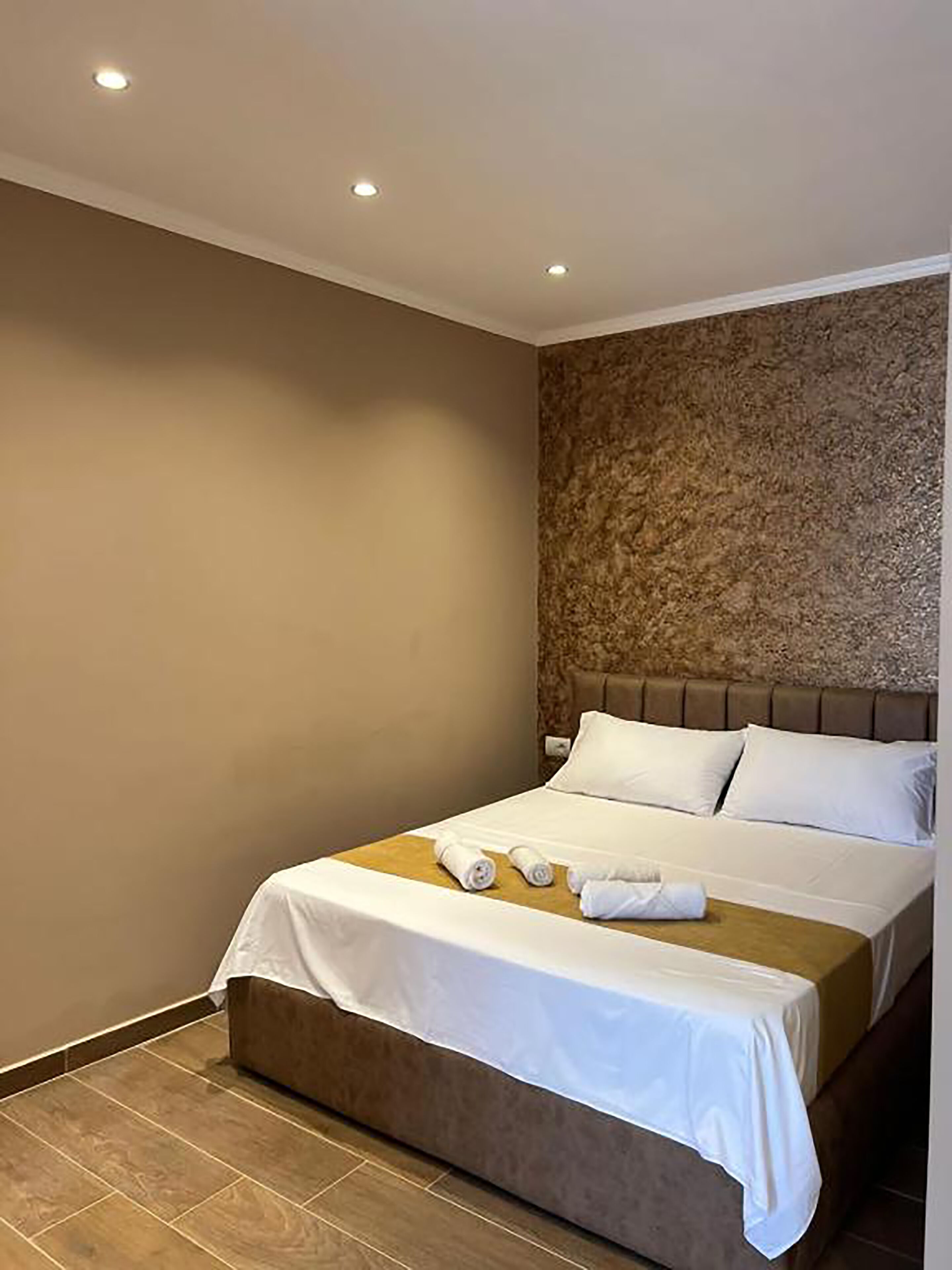 A hotel room with a bed, a headboard, and a wall with a textured pattern.