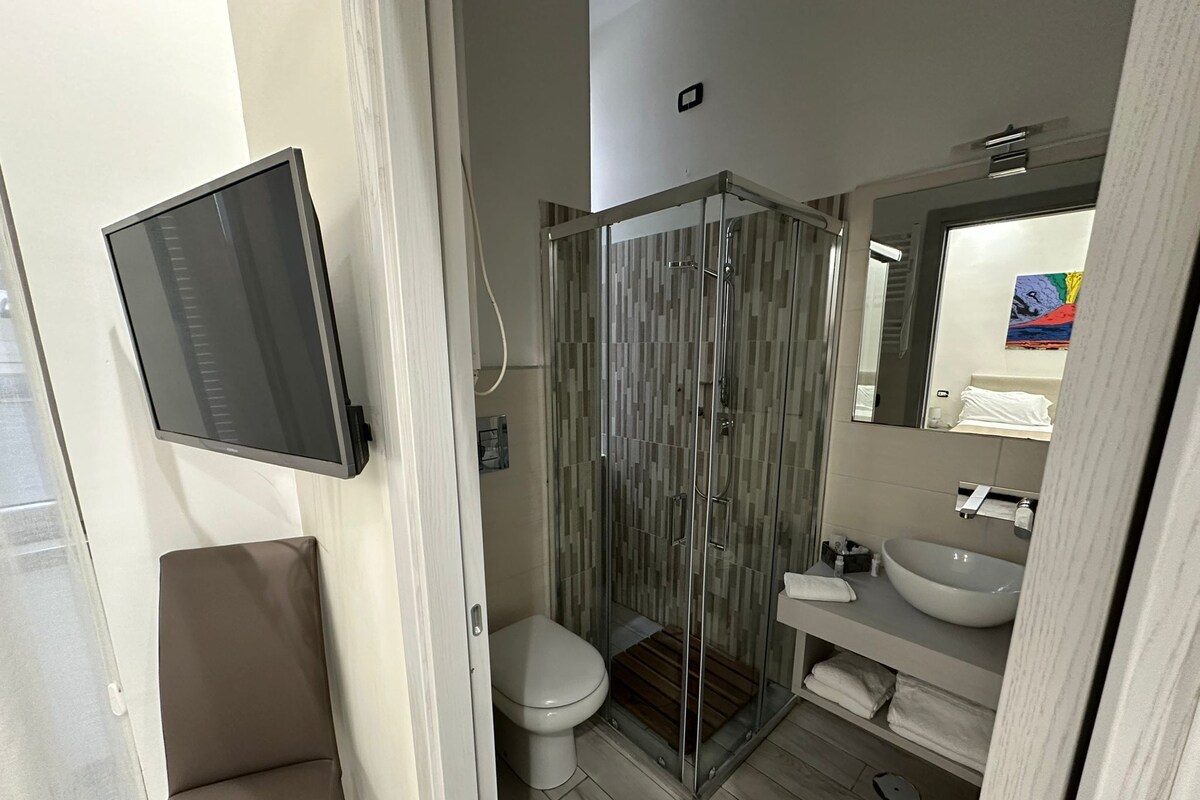 A modern bathroom with a glass shower enclosure, a toilet, a sink, and a mounted television.