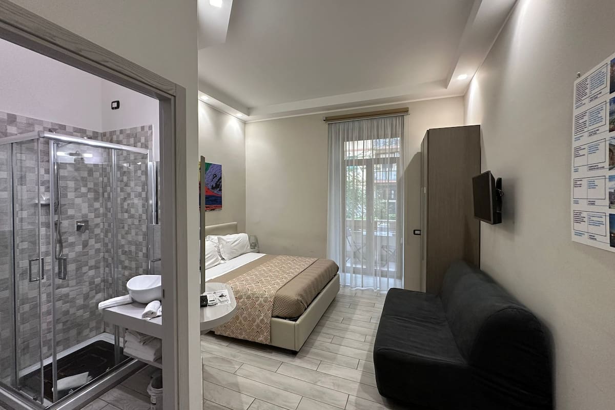 Ein modernes Hotelzimmer mit Dusche, WC, Bett und einer Sitzecke.