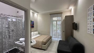 A modern hotel room with a shower, toilet, bed, and a seating area.