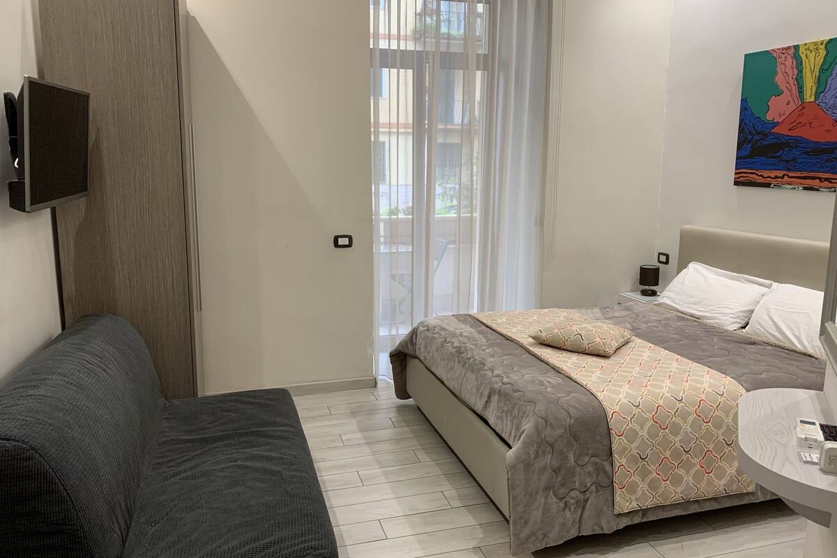 Ein modernes Schlafzimmer mit einem Bett, einer Couch, einem Fernseher und einem Bild an der Wand.