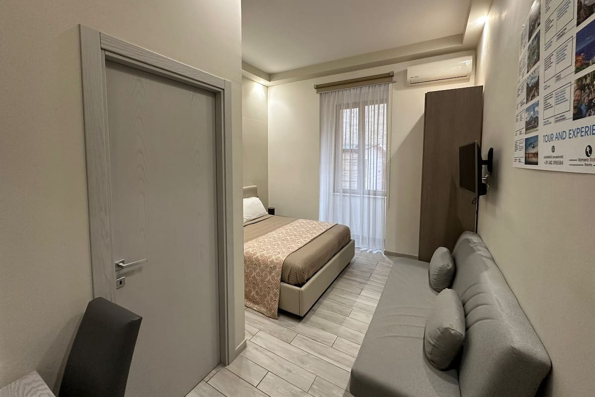 Ein Hotelzimmer mit einem Bett, einer Couch, einer Tür und einem an der Wand montierten Fernseher.