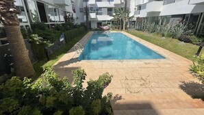 Una piscina rodeada de un jardín con diversas plantas y una palmera.