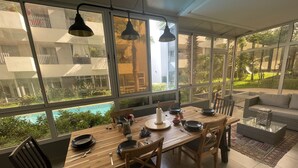 Un comedor con mesa de madera, sillas y vistas a una piscina y follaje exterior.