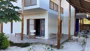 Un bâtiment moderne à deux étages, doté d’un balcon, d’un espace extérieur couvert aménagé en coin salon et d’une terrasse dallée.