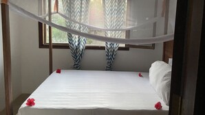 Un lit avec une literie blanche et des fleurs rouges, une fenêtre avec des rideaux à motifs et une moustiquaire au-dessus.