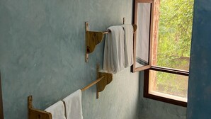 Une salle de bain avec un porte-serviettes en bois, une fenêtre donnant sur la verdure et un luminaire au plafond.