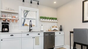 Una cocina moderna con armarios blancos, lavavajillas, cafetera y ventana con persianas.