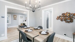 Un comedor con una mesa de madera dispuesta para cuatro, una araña y una obra de arte en la pared.