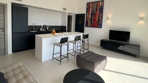 A modern kitchen with a central island, bar stools, a flat-screen TV, and a large abstract painting. - Large 2-room apartment with panoramic sea view (Rayol-Canadel-sur-Mer)