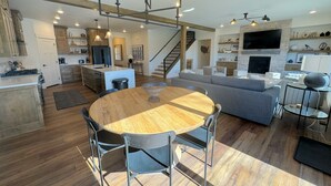 Amplio espacio de sala con una mesa de comedor de madera, sofá gris y un televisor instalado en una pared de piedra.