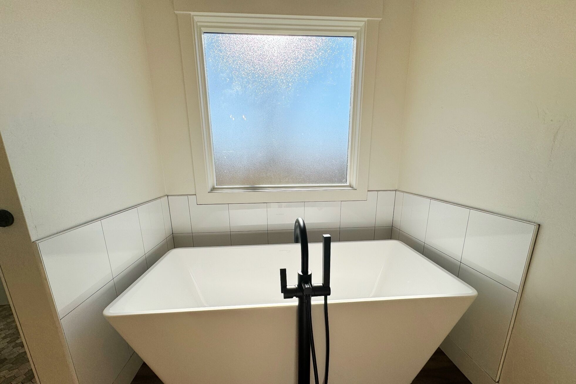 Ein kleines Badezimmer mit einer weißen Badewanne, einem Fenster darüber und weiß gefliesten Wänden.