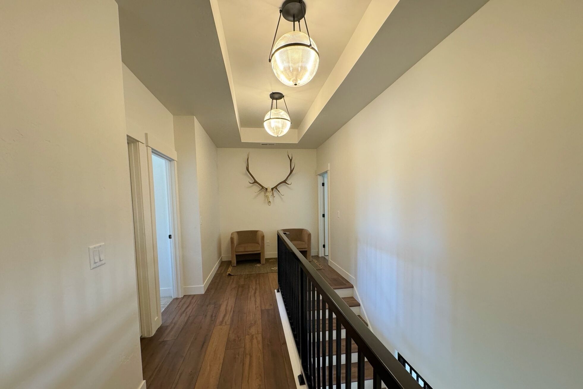 A hallway with wooden flooring, a black railing, and a chandelier.