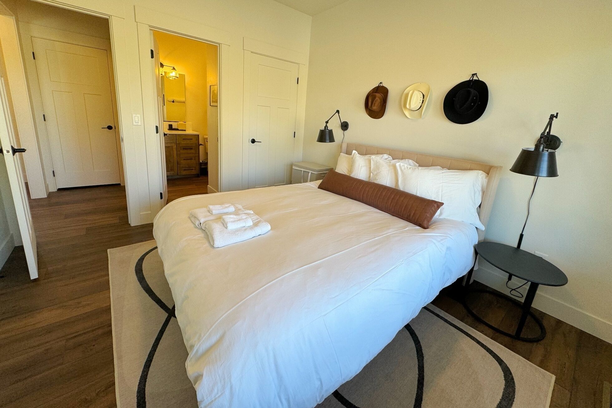 Une chambre d’hôtel avec un grand lit, une table de chevet, une lampe et un porte-chapeau fixé au mur.