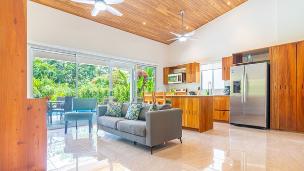 A modern kitchen with wooden cabinets, a stainless steel refrigerator, and a dining area with a sofa and chairs. - Two bedroom. Ojochal. Private pool. Minutes to beach (Ojochal)