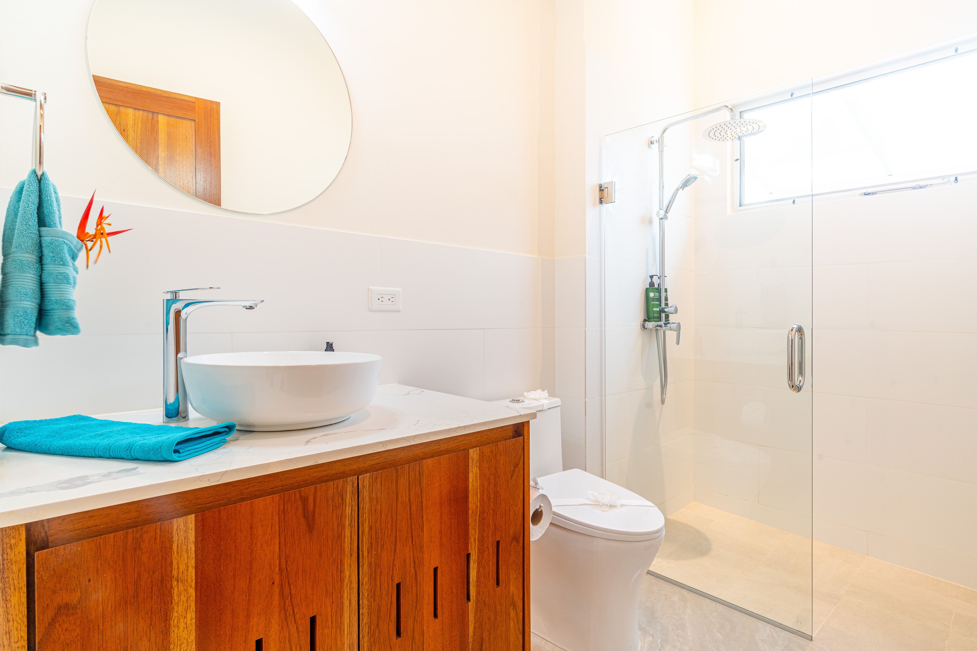A modern bathroom with a wooden vanity, a white sink, and a glass-enclosed shower.