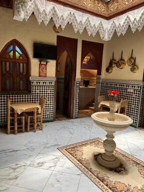 A room with a dining area featuring a table and chairs, a decorative fountain, and a tiled floor with a patterned rug. - Riad Elijah (Marrakech)